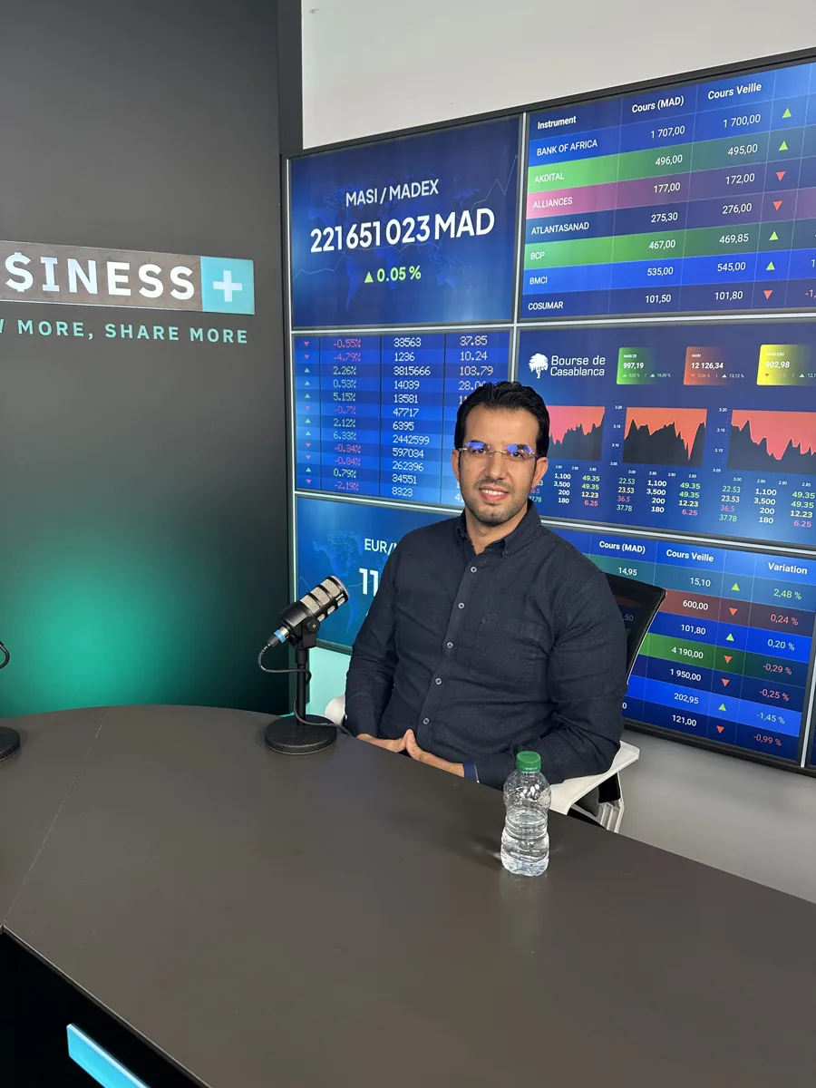 Dr CHARRASS Abdelmajid sur le plateau de Business+, devant des écrans de cotations boursières