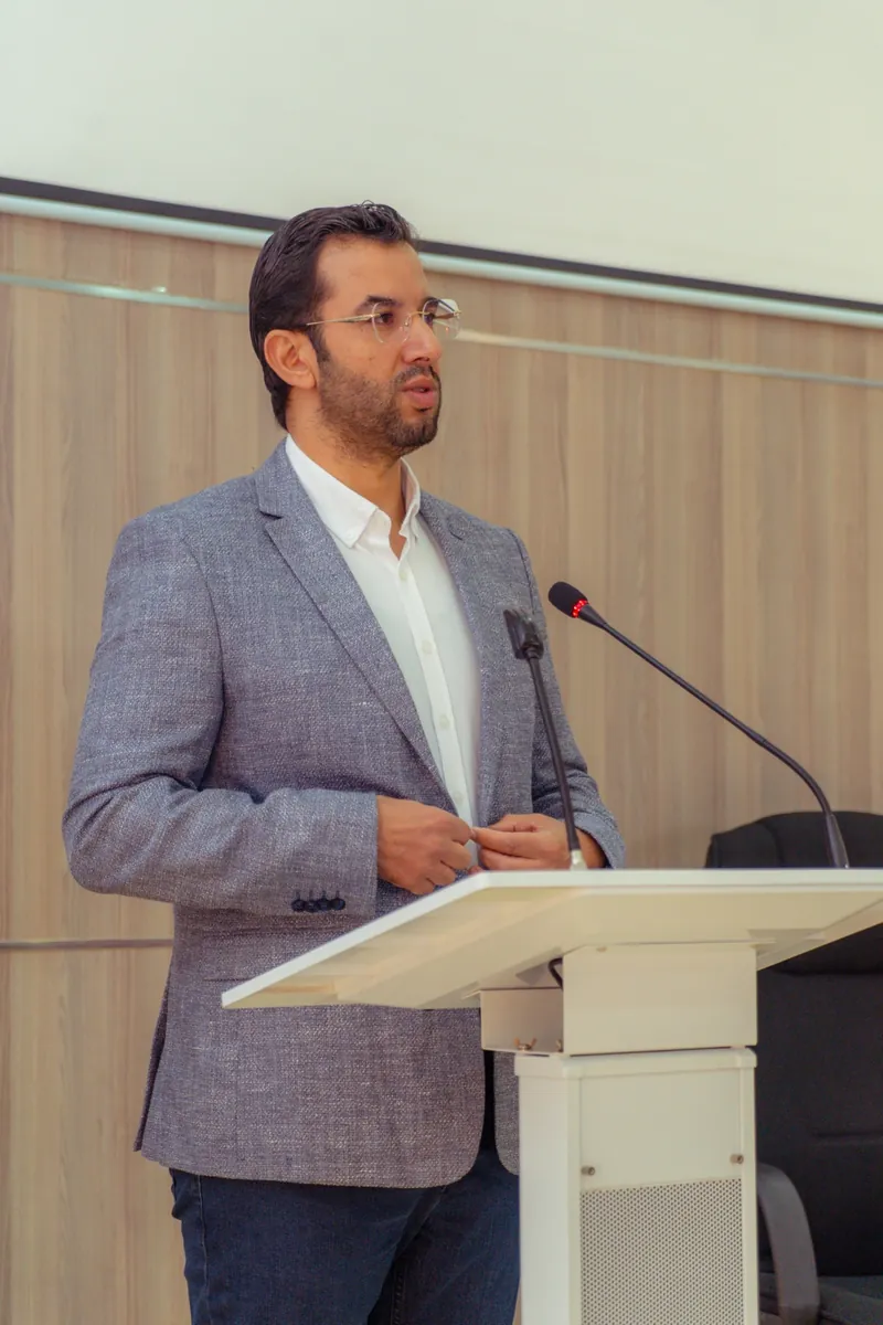 Abdelmajid Charrass debout à un pupitre et parlant dans deux microphones.