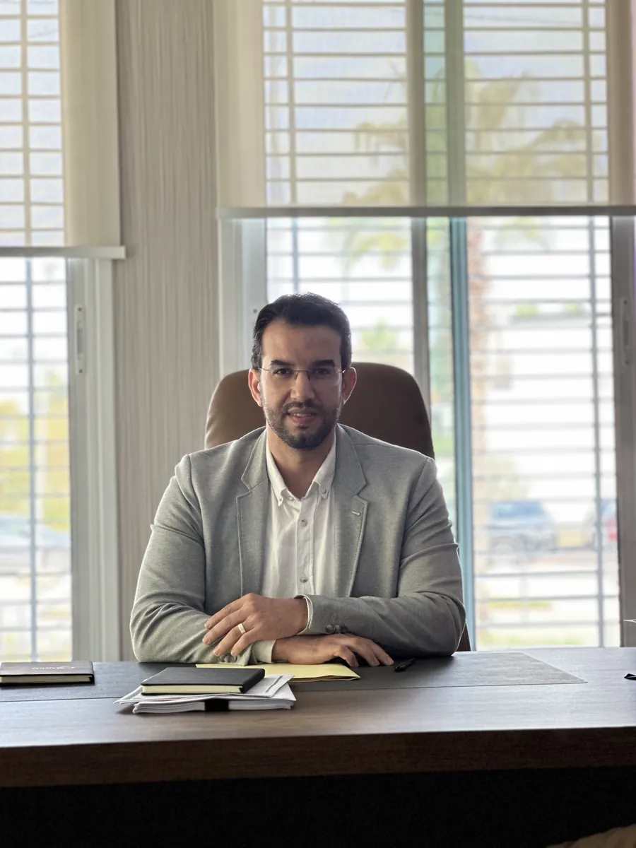 Dr CHARRASS Abdelmajid assise face a l’objectif derrière un bureau, veste grise.