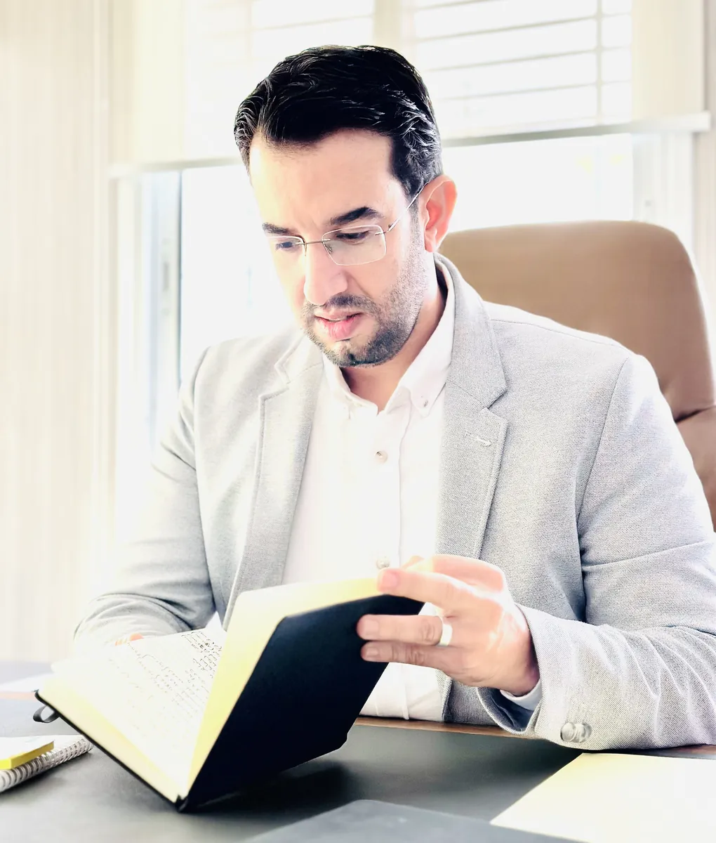 Abdelmajid Charrass en veste grise lisant un livre ouvert a son bureau.