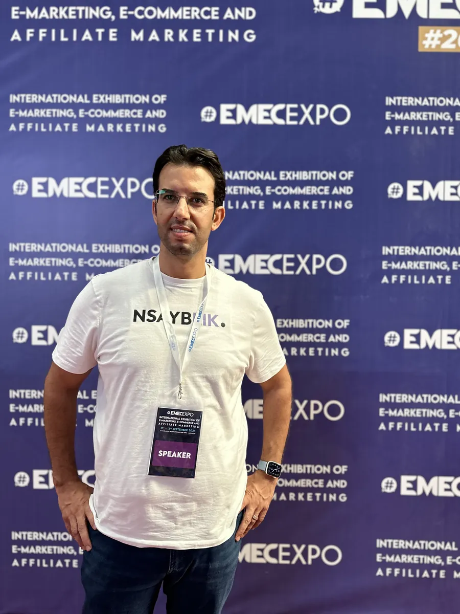 Abdelmajid Charrass, badge intervenant, devant le panneau du salon EMEC Expo